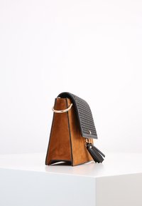 Borsa a tracolla nera in pelle perforata con corpo in suede color cuoio, forma triangolare, hardware dorato e una nappa decorativa sul lato.
