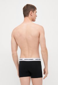 Schwarze Boxershorts mit einem weißen elastischen Bund, der das Logo "JACK & JONES" zeigt; von hinten vor einem schlichten Hintergrund dargestellt.