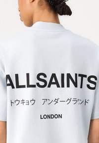 Lys blå kortermet T-skjorte med "ALLSAINTS" og japansk tekst i fet svart skrift på baksiden, laget av myk bomull.