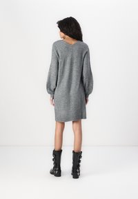 Robe en tricot grise avec une coupe décontractée, des manches bouffantes et un décolleté en V, accompagnée de bottes noires hautes avec plusieurs boucles en argent.
