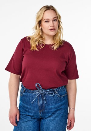 Bordeaux-rotes geripptes T-Shirt mit kurzen Ärmeln, kombiniert mit hoch taillierten blauen Denim-Jeans, die eine gebundene Schleifendetail an der Taille aufweisen.
