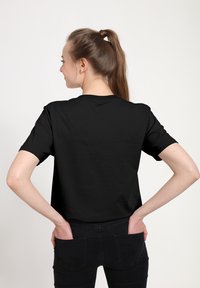 Černé bavlněné tričko s krátkými rukávy, kulatým výstřihem a volným střihem, nošené s odpovídajícími černými džínami. Hladká textura, minimalistický design.