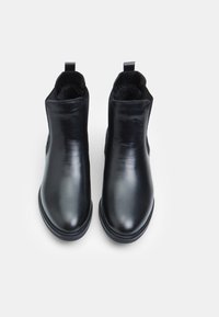 Botas de cuero negro hasta el tobillo con un acabado suave, punta redondeada, paneles laterales elásticos y lengüetas para ponerlas y quitarlas fácilmente. Suelas de goma planas.