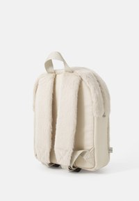 Faux fur backpack in cream with padded fabric, rectangular shape, and adjustable straps. Features a top loop for hanging.