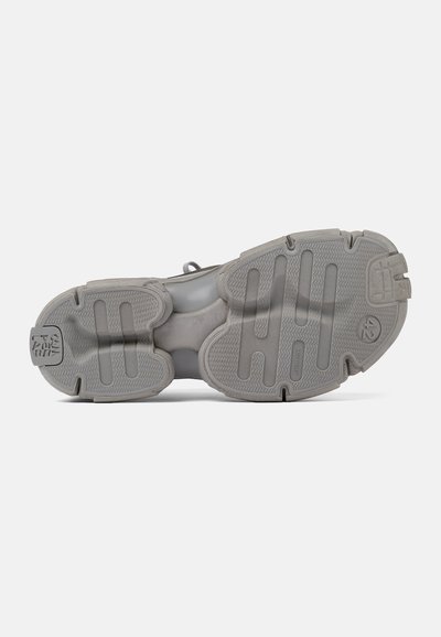 Sole di sneaker grigia con battistrada in gomma testurizzata, caratterizzata da scanalature e dettagli decorativi per una migliore aderenza. Allineamento centrale con un design minimalista.