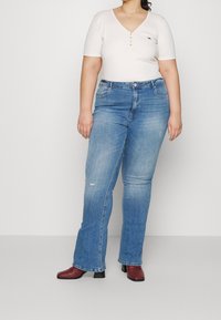 Bílý proužkovaný top s krátkým rukávem a výstřihem do V, doplněný o modré zničené džíny s rovnými nohavicemi a červené kotníčkové boty.