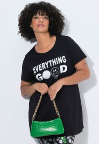 Czarny t-shirt z białym napisem „EVERYTHING GOOD”, zestawiony z błyszczącą zieloną torebką o wzorze krokodyla i złotym łańcuszkowym uchwytem.