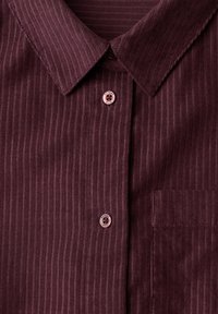 Chemise en velours côtelé marron rouge avec col pointu, rayures verticales, boutons sur le devant et poche poitrine côté droit.