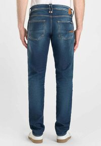 Jeans de mezclilla azul oscuro con corte slim, que cuentan con dos bolsillos traseros con detalles de costura y un parche de cuero con el logotipo en la cinturilla.