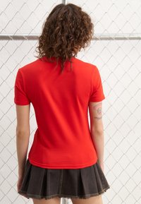 Camiseta de algodón roja con manga corta y escote redondeado, combinada con una falda de pliegues color carbón con dobladillo sin terminar.