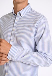 Overhemd met knopen in blauw en wit gestreept ontwerp, gemaakt van stof met een gladde textuur. Opvallende details zijn een traditionele kraag en knopenmanchetten.