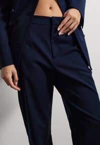 Pantaloni eleganti blu navy, realizzati in tessuto liscio, presentano tasche laterali e una parte anteriore piatta con una finitura pulita, completati da una vita aderente.