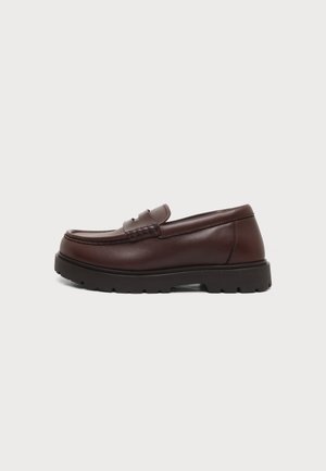 Brun læderloafer med sort chunky sål og moc tå-syning, vist i sideprofil på en hvid baggrund.