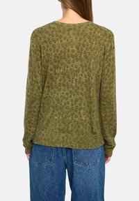 Zielona oliwkowa sweter z teksturalnym, kropeczkowym wzorem, prążkowanym dekoltem i mankietami. W stylizacji z luźnymi, niebieskimi dżinsami.
