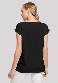 T-shirt noir à manches courtes avec une coupe décontractée, en tissu doux et avec des manches retroussées. L'arrière est légèrement plus long, associé à un pantalon de couleur claire.