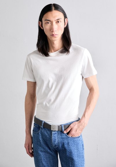 White short-sleeve t-shirt paired with blue patterned jeans, featuring a gray belt with a metallic clasp and a smooth fabric texture.