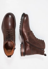 Bruna läder- och mockaboots till anklarna med snörning fram och dragkedja på sidan. Rund tå, texturerad yta och robust sål.