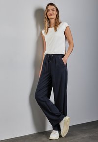 Løse navy bukser med elastisk talje og snor, parret med en hvid kortærmet top. Sættet inkluderer hvide sneakers.