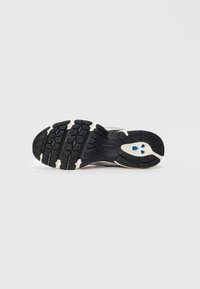 Semelle de sneaker New Balance en noir et blanc avec un motif de semelle texturé et trois petites formes bleues près du talon.