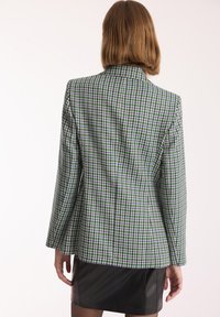 Marynarka w wzór houndstooth w zielonym, czarnym i białym kolorze, o dopasowanym kroju i długich rękawach, z klasycznym kołnierzem i usztywnioną konstrukcją.