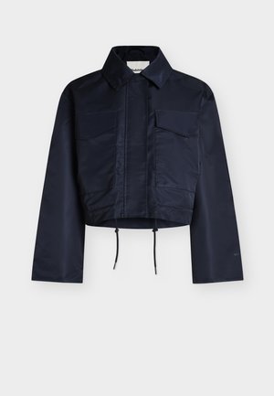 Σκούρο μπλε κοντό μπουφάν με μακριά μανίκια, μυτερό γιακά, δύο τσέπες στο στήθος με καπάκια και ρυθμιζόμενα κορδόνια στο τελείωμα.