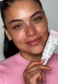Too Faced Hangover primer in a pink and white tube with vintage-style label. Model features a ribbed pink top and glossy lips.
