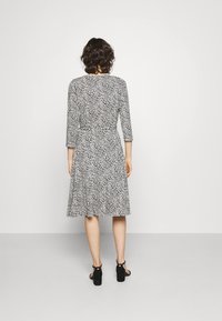 Schwarz-weiß gemustertes Kleid mit Dreiviertelärmeln, gerafftem Taillenteil und schwingendem Rock, kombiniert mit schwarzen Absatzsandalen.
