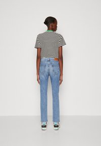 Ribaga must-valge T-särk, sinised teksad tagataskute ja mitmevärvilised tossud. Kitsas lõige, keskmise värvuse denim, õmblemise detailid.