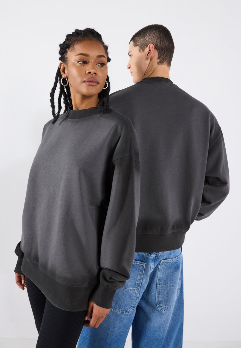 Mørkegrå sweatshirt med høy utringning, senkede skuldre og ribbestrikkede mansjetter. Den har en avslappet passform og glatt tekstur, båret av to modeller.