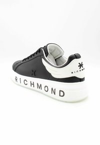 Zapatilla Richmond en blanco y negro con detalle de ala en el talón, cordones negros y la palabra "RICHMOND" impresa en negro sobre una suela blanca gruesa.