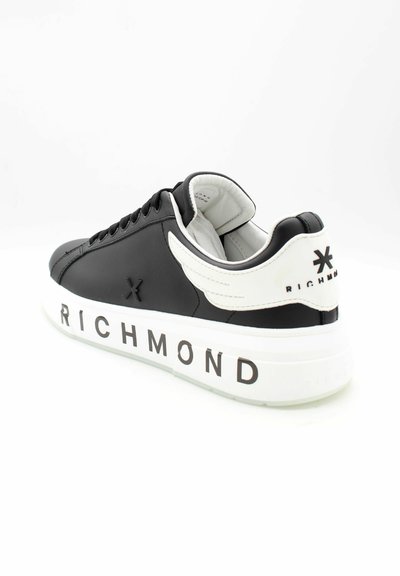 Zwart-witte Richmond sneaker met vleugeldetail op de hiel, zwarte veters en "RICHMOND" in het zwart gedrukt op een dikke witte zool.