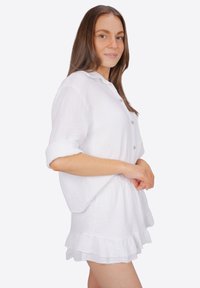 Chemise blanche à boutons avec manches retroussées, faite d'un tissu texturé. Associée à une jupe à volants superposés, le tout dans une coupe ample.