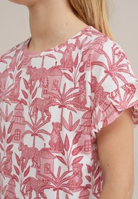 Bela majica s kratkimi rokavi z vzorcem rožnatega leoparda in tropskega listja; ima okroglo ovratnico in naborke na robovih rokavov.