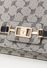 Patterned handbag in cream and black with a textured finish, featuring a gold-tone clasp and black leather accents.