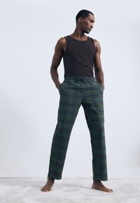 Pyjamabroek van groene plaidstof met marineblauwe accenten, met een elastische tailleband en zijzakken. Gecombineerd met een zwarte tanktop.