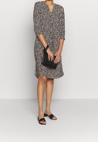 Blommönstrad klänning med mörk bakgrund, V-ringning, trekvartsärmar och knälång fåll; ihop med en svart handväska och sandaler.