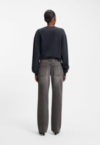 Oversized marinblå sweatshirt kombinerad med löst sittande, gråa denimbyxor. Jeansens baksida har två fickor och en subtil falning i tyget.