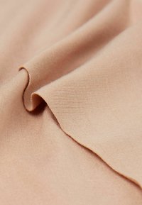 Perzikkleurige stof met een gladde textuur en een lichte glans, met subtiele ribbels en een zachte val. Randen zijn licht gekruld en gelaagd.