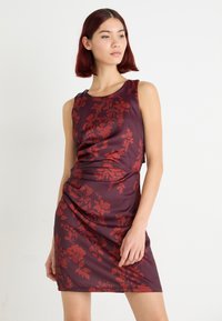 Robe bordeaux élégante avec des motifs floraux rouges, sans manches et à la silhouette ajustée. La texture lisse renforce l'aspect élégant.