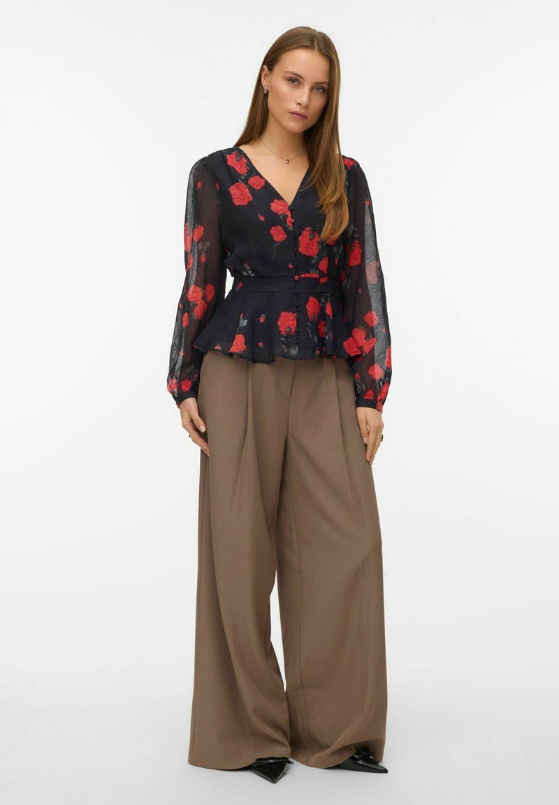 Peplum-paita läpinäkyvässä mustassa kankaassa, jossa on punaisia kukkakuoseja, V-kaula-aukko, pitkät hihat ja napit edessä; yhdistetty leveisiin beigenvärisiin housuihin.