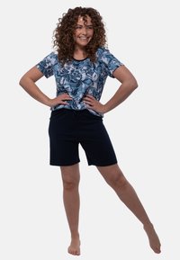 Outfit informale con una maglietta a maniche corte a motivo floreale blu e bianco, abbinata a pantaloni corto blu scuro, il tutto in un tessuto leggero.