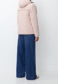 Helle rosa Pufferjacke mit Kapuze, in lockerer Passform, mit horizontalen Nahtdetails und getragen über weit geschnittenen blauen Jeans.