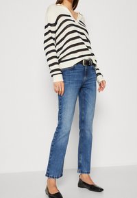 Randig tröja i cream och marinblå, gjord av stickat material; parat med blå denimjeans; accessoriserad med ett svart bälte och platta skor.