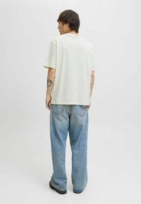Tricou din bumbac alb-crem, cu o croială lejeră, mâneci scurte și decolteu rotund, asortat cu blugi deschiși la culoare, cu talie înaltă.