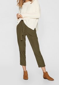 Olijfgroene tapered broek met een drawstring. Gecombineerd met een crèmekleurige gebreide trui. Beige enkellaarzen zichtbaar onderaan.