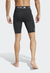 Crne atletske šortse sa prilagođenim dizajnom, s bijelim bočnim prugama i širokim pojasom na kojem je označeno "TECHFIT" i "Adidas."