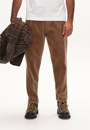 Brown corduroy pants with vertical stripes, paired with a textured brown jacket, and black boots with yellow laces, held in the left hand.