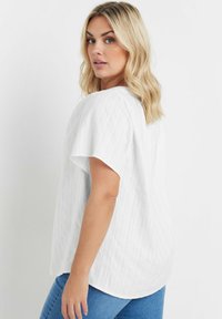 Top corto bianco a maniche corte con un design a righe testurizzate, orlo arrotondato e vestibilità rilassata, abbinato a jeans in denim blu.