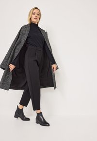Bottines noires à talon carré, col roulé noir ajusté et manteau gris à motifs. Le manteau a un extérieur texturé et de larges revers.