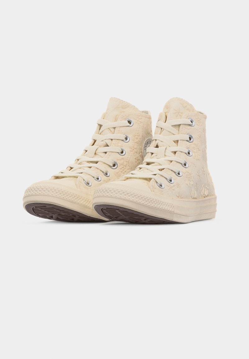 Paar cremefarbene High-Top-Sneaker mit floralem Strukturmuster, weißen Schnürsenkeln und Gummisohlen, leicht nach links geneigt auf weißem Hintergrund.